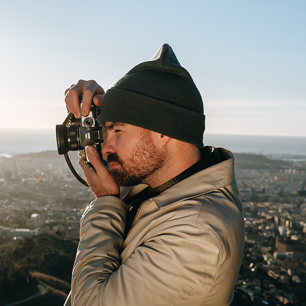 A photographer is holding the Olympus O-M3 mirrorless camera with the Olympus M.ZUIKO DIGITAL 17mm F1.8 II lens attached to the camera body.