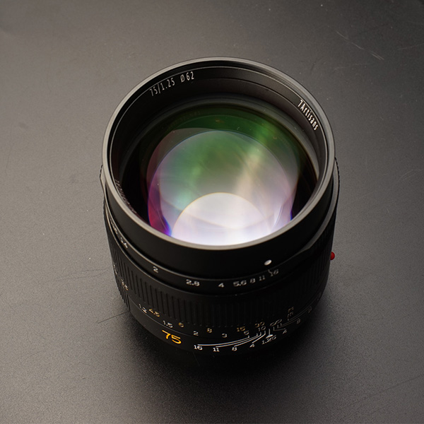 This is the 7artisans 75mm f/1.25 lens for Leica M-mount cameras viewed from the front and at a slight angle on a dark gray background.